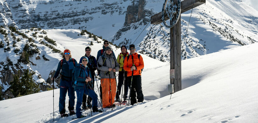 A group of snowshoe hikers reach the cross at the Plumssattel and enjoy their summit happiness.