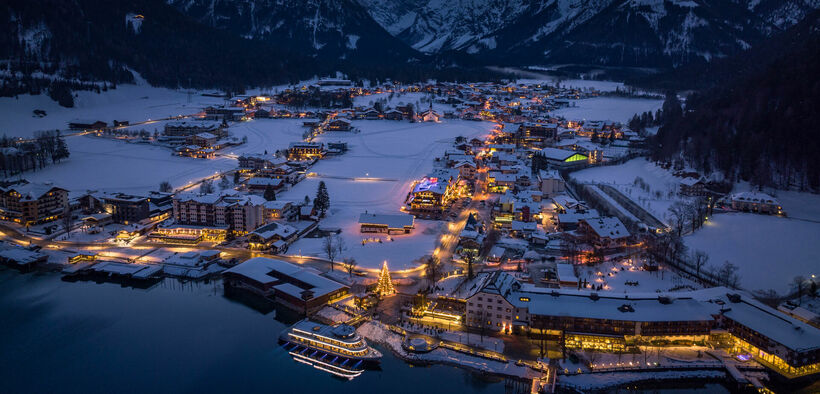 Night shot of the snow-covered village of Pertisau am Achensee in the Advent season, festooned with decorations and sparkling lights.