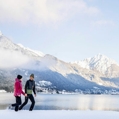 Winter walk in Pertisau am Achensee A couple enjoying a winter walk in the snowy landscape of Lake Achensee, backdropped by Maurach and the Ebner Joch.