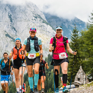 Eine Gruppe Teilnehmer des Karwendelmarschs wandern über einen steinernen Pfad vor schöner bergiger Kulisse und bewölktem Himmel.