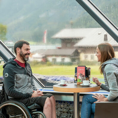 Two friends chat over a hot drink at Café Vitalberg. The bar is accessible barrier-free via the panoramic lift.