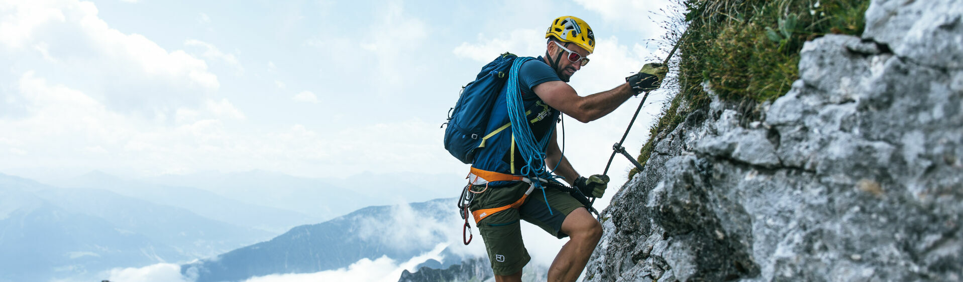 Ein Mann auf einem Klettersteig im Rofangebirge bei blauem Himmel mit vereinzelten Wolken.